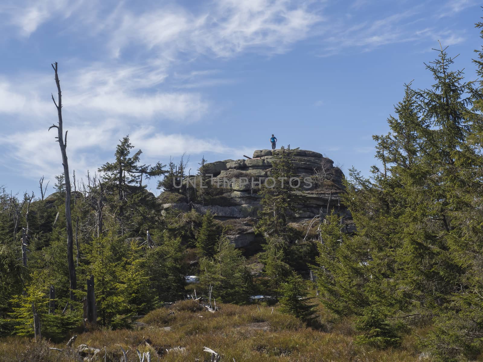 Jizera Mountains jizerske hory landscape, view on holubnik and men staning on the top of the mountain with lush green spruce forest, trees, boulders and blue sky background, springtime .