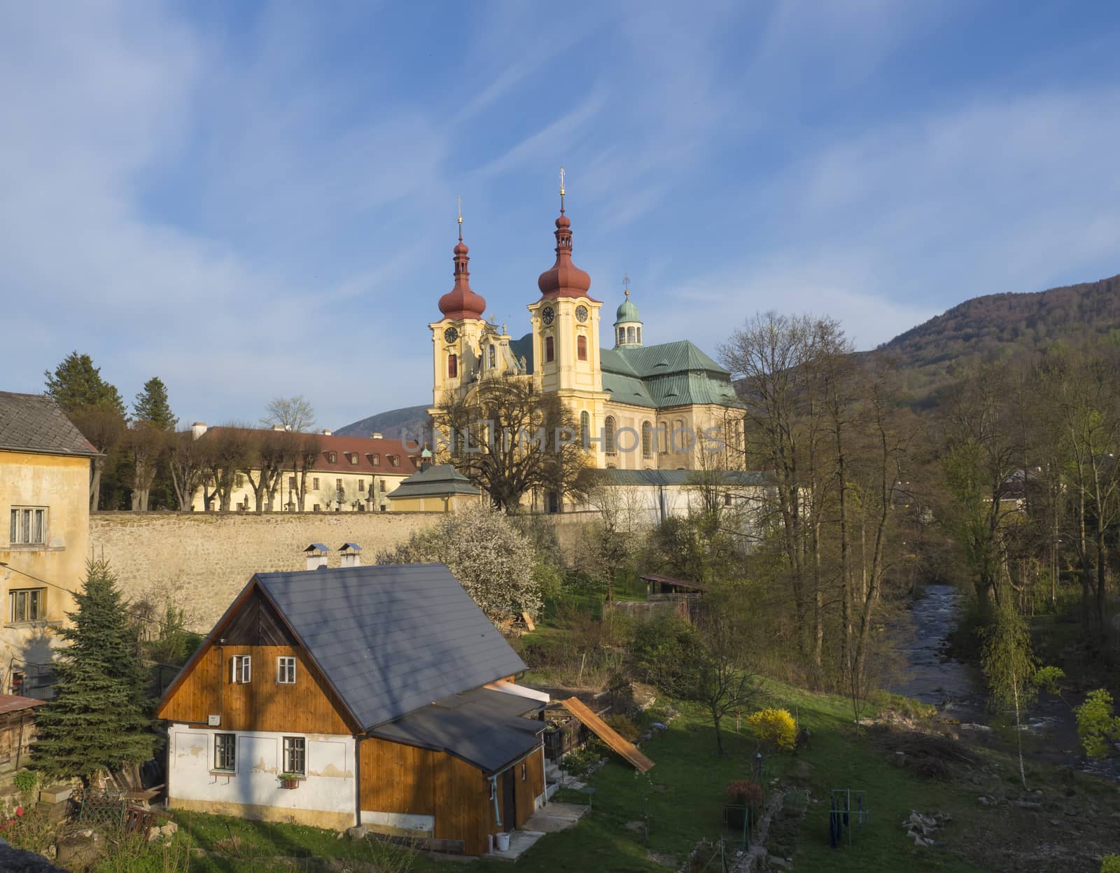 View on Village Hejnice with cottages, creek and Baroque Basilica church of the Visitation Virgin Mary in spring, golden hour light, place of pilgrimage, Hejnice, Jizera mountain, Czech Republic, spring