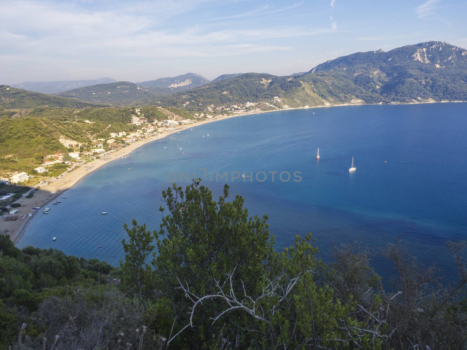 Panoramic view of Agios Georgios Pagon sand beach with green hills and sailing ships at Corfu island, Greece, sunny day blue sky.