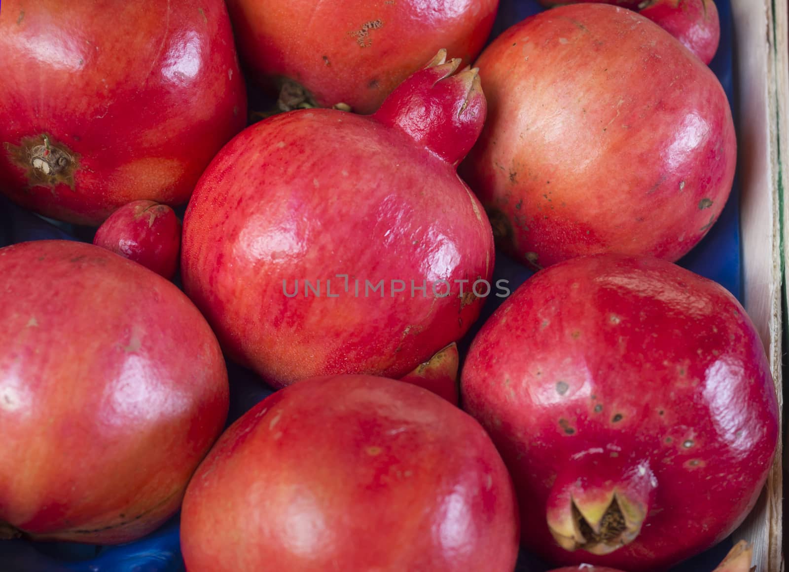 Close up red ripen whole Pomegranate fruits in wooden box. Tropical fruit background. Organic Bio fruits, selective focus.