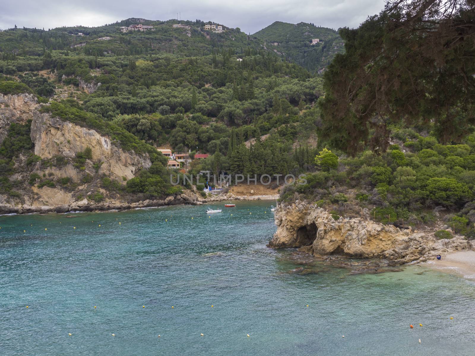 View on cllif and cave, trees and green hill at Paleokastritsa bay with two small boats summer cloudy sky, Corfu, Greece.