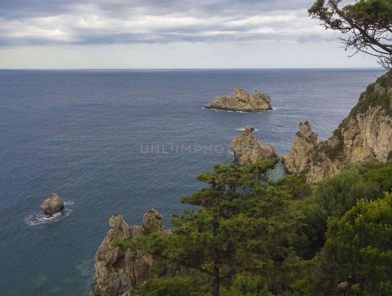 View on cllifs, trees and green hill at Paleokastritsa bay, summer cloudy sky, Corfu, Kerkyra, Greece.