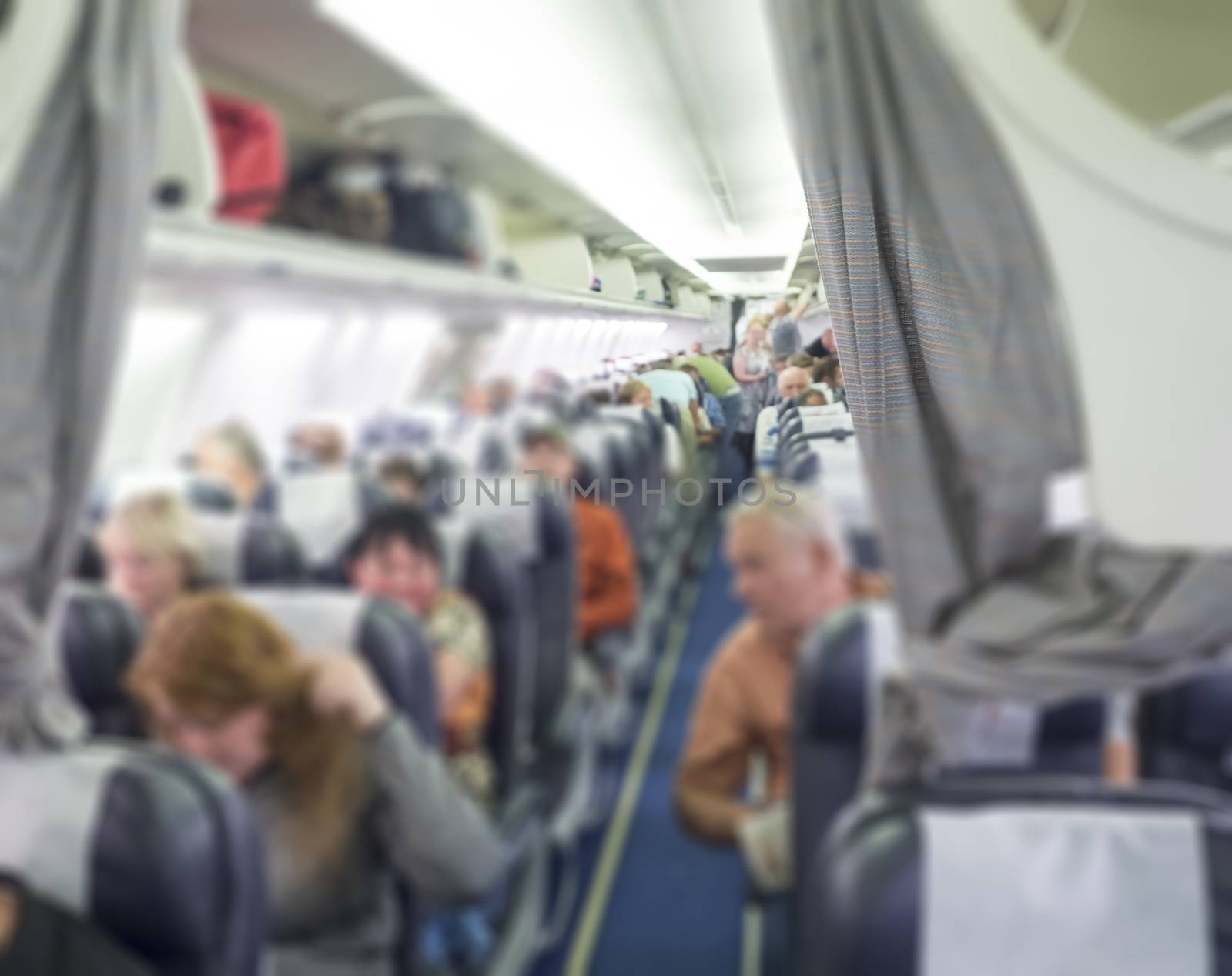 Blurred background of interior of commercial airplane, selective focus and diminishing perspective, passengers sitting on the economy class on charter holiday flight. Air transport is the current popular and fast by Henkeova