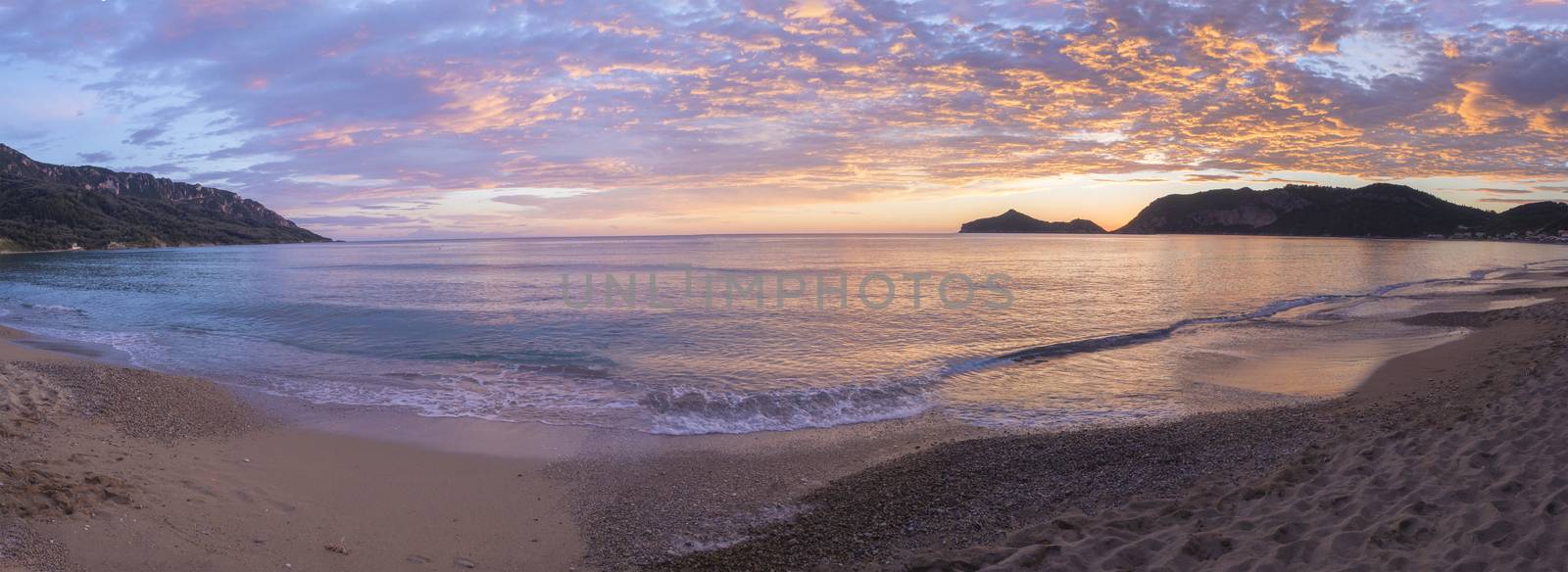 Panoramic view on beautiful pastel pink orange and golden sunset clouds and waves at sea shore Agios Georgios Pagon beach at Corfu island, Greece.
