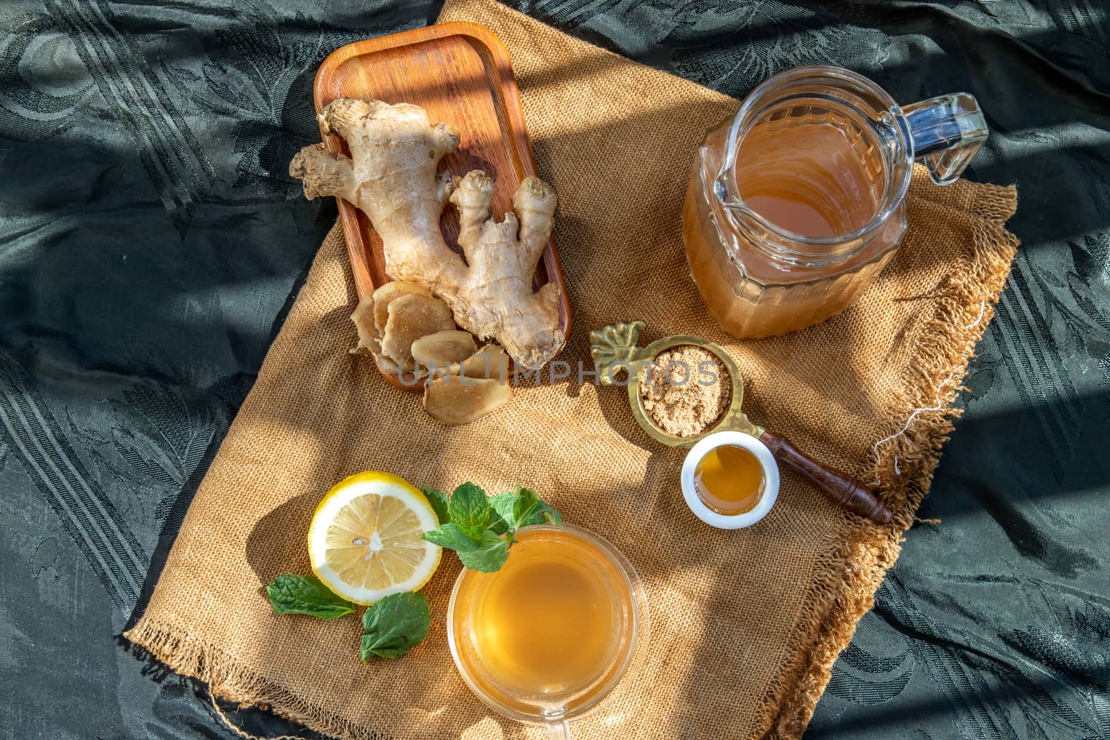 Hot Ginger juice with lemon and mint, root and slices of ginger Served with brown sugar and honey on sackcloth background. Hot ginger juice can helps warming body, Healthy Drink.