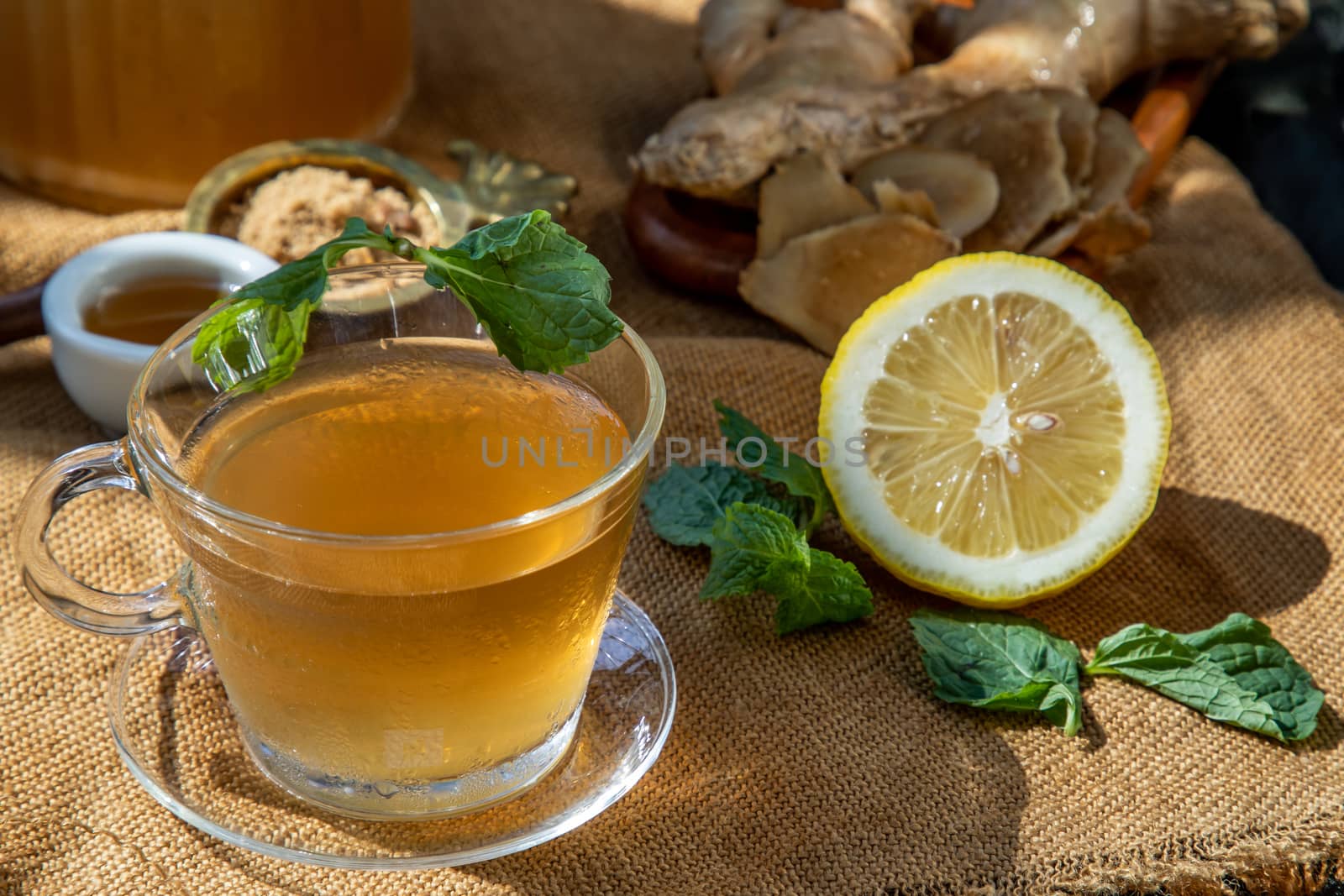 Hot Ginger juice with lemon and mint, root and slices of ginger Served with brown sugar and honey on sackcloth background. Hot ginger juice can helps warming body, Healthy Drink.