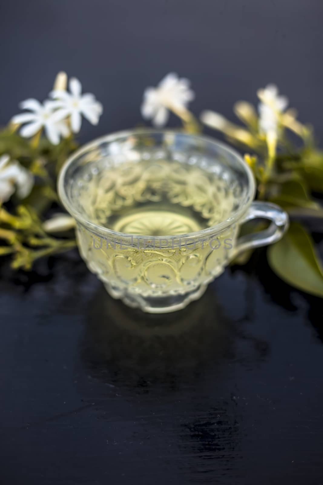 Close up of tea of Indian jasmine flower or juhi or Jasminum Auriculatum on wooden surface in a glass cup with raw flowers.