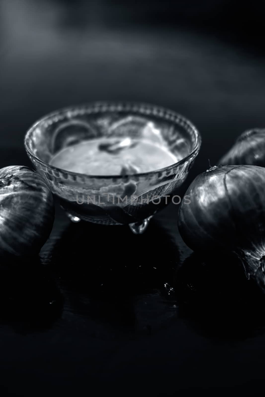 Close up of glass bowl full of extracted onion pulp in it and raw onions or pyaaj or Allium cepa.