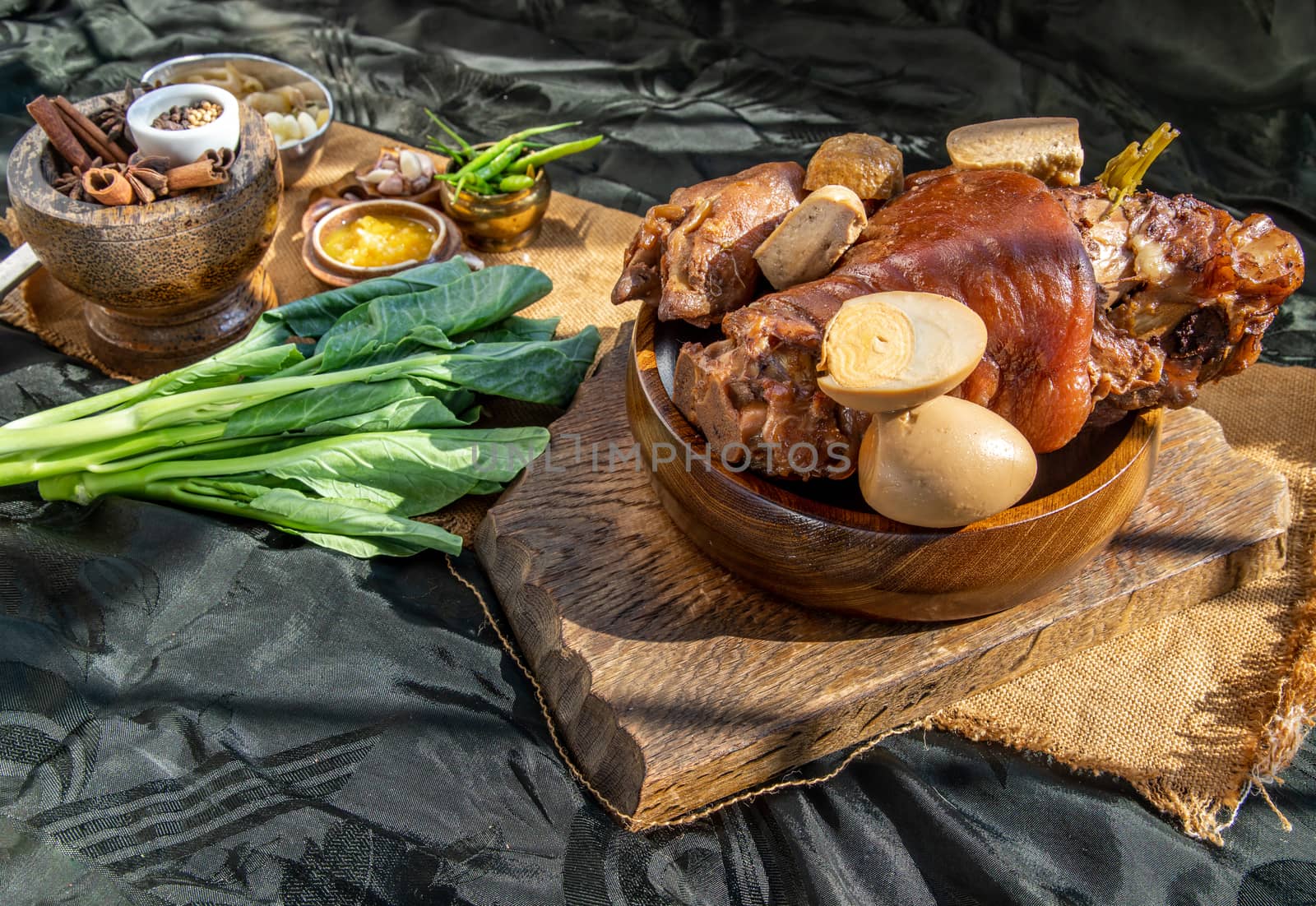 Chinese traditional dish Stewed pork leg with boiling sweet gravy sauce and boiled egg, tofu, kale Served with Pickled Lettuce and pickled chilli on black background. Selective focus.