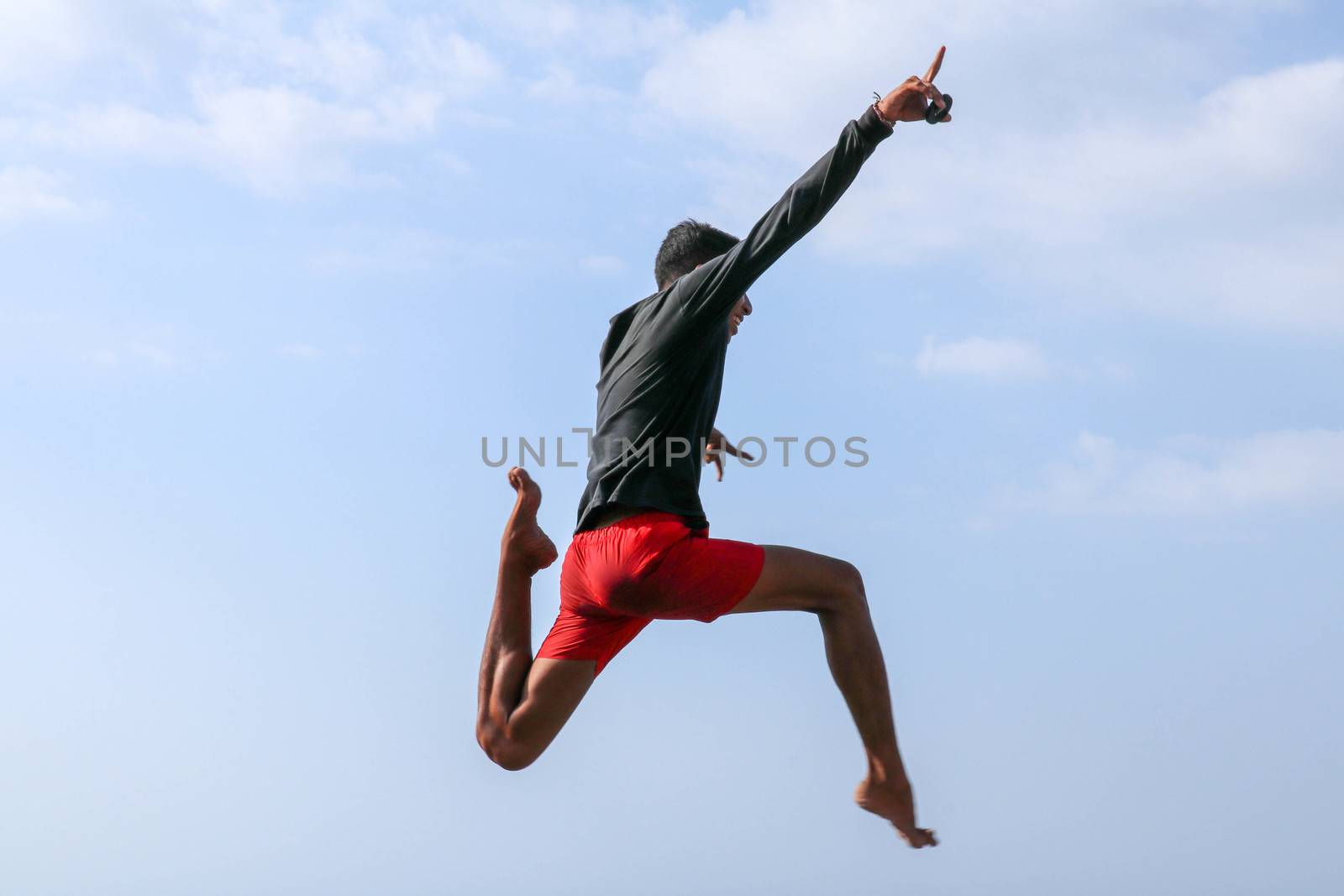 Man jumping happy in the beach with a blue sky in the background. Young cheerful Indonesian jumps. A teenager in a good mood jumps in the air. Background with blue sky. Sunny tropical day.