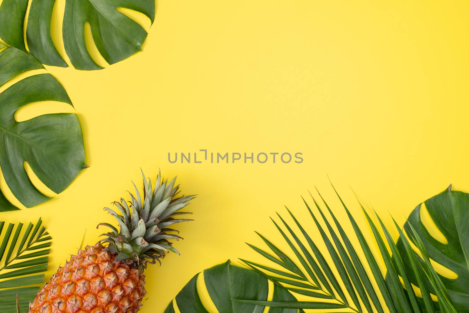 Beautiful pineapple on tropical palm monstera leaves isolated on bright pastel yellow background, top view, flat lay, overhead above summer fruit.