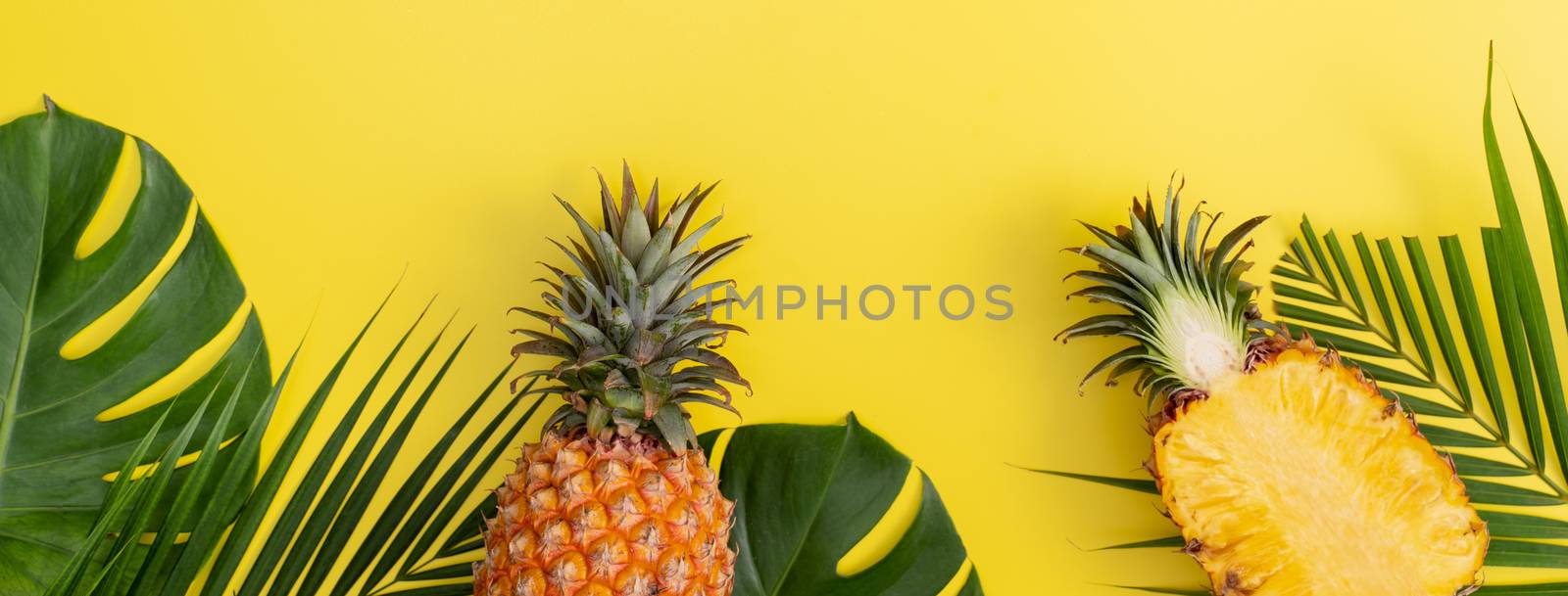 Beautiful pineapple on tropical palm monstera leaves isolated on bright pastel yellow background, top view, flat lay, overhead above summer fruit.