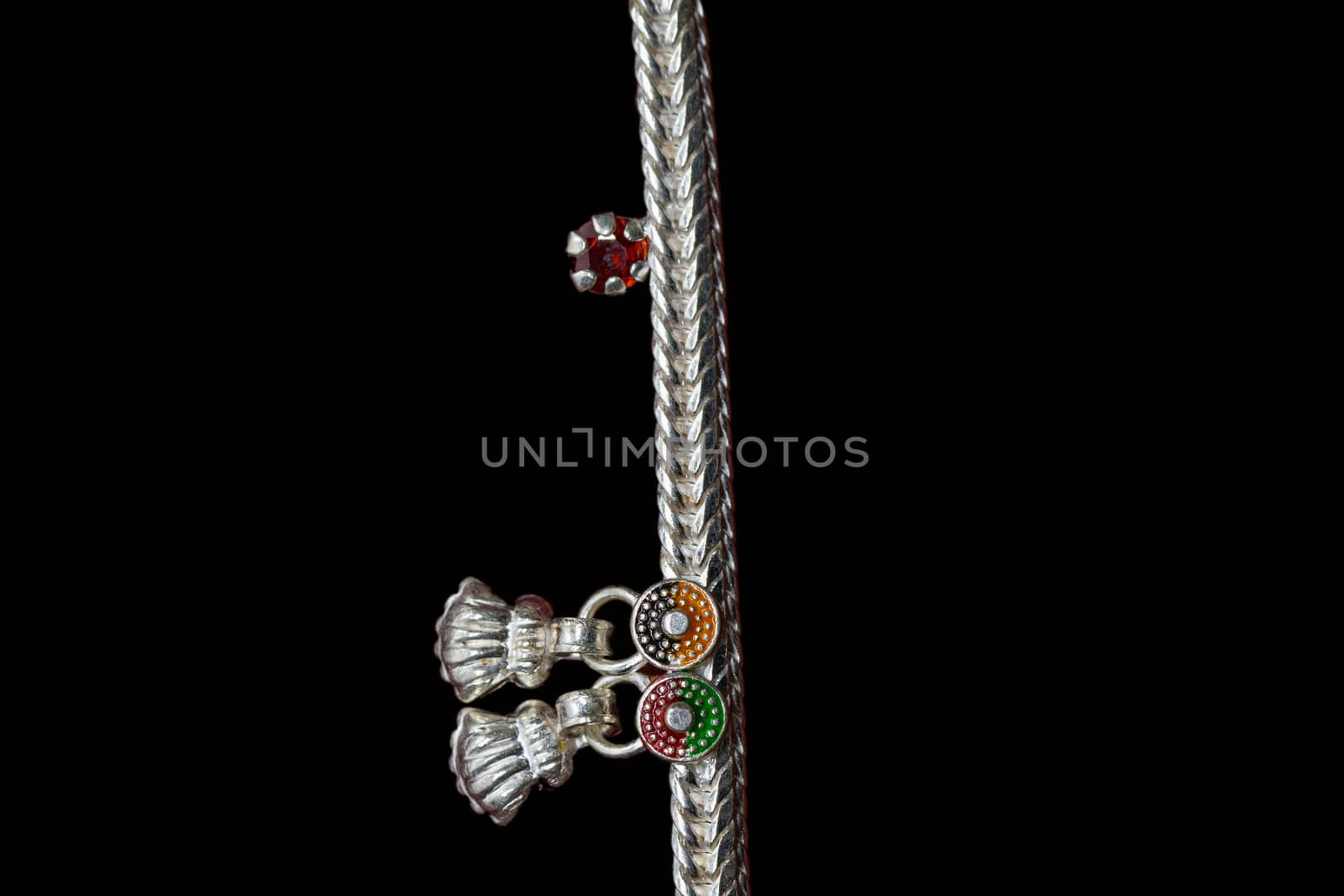 Beautiful silver anklet is curled up with on red stone on the black background