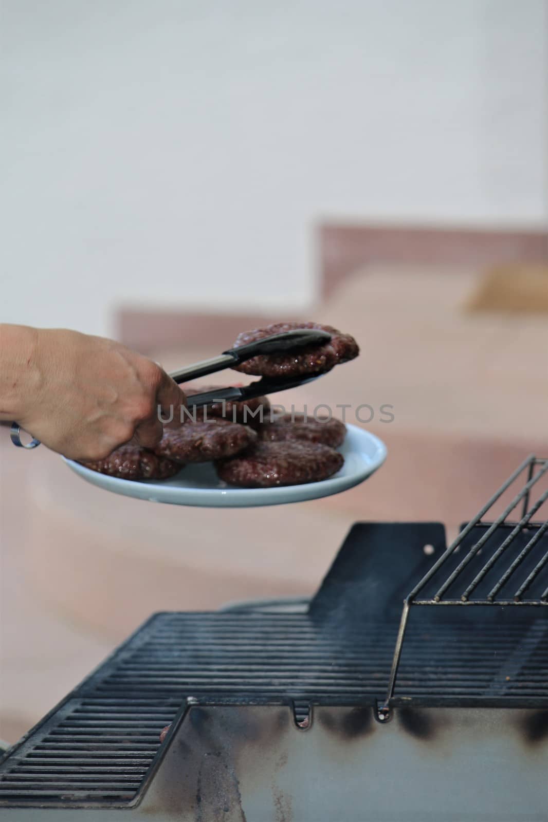 One hand uses a pair of tongs to place burgers on a plate