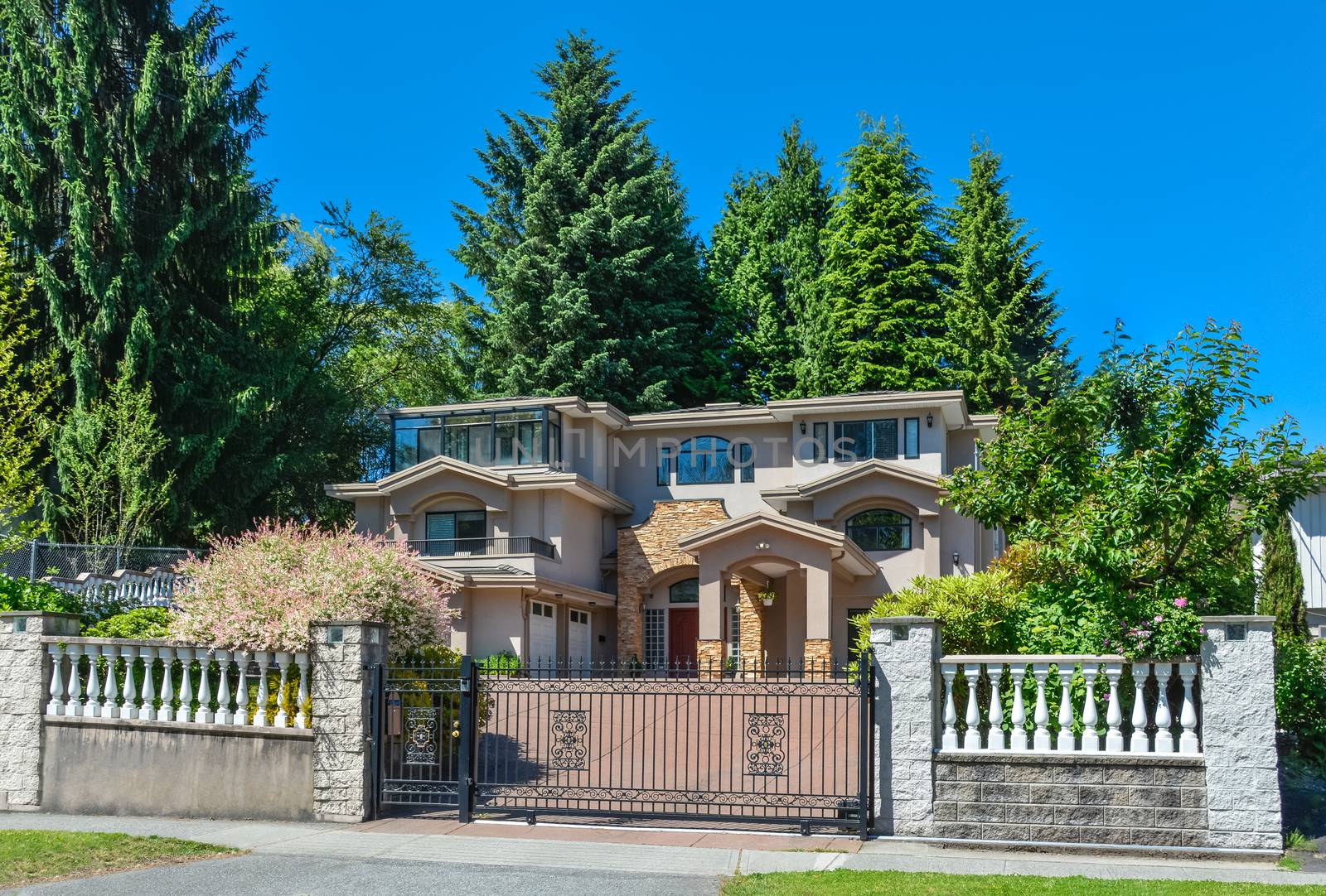 Luxury residential house with double garage and metal gate in front. Beautiful house in suburb of Vancouver on blue sky background