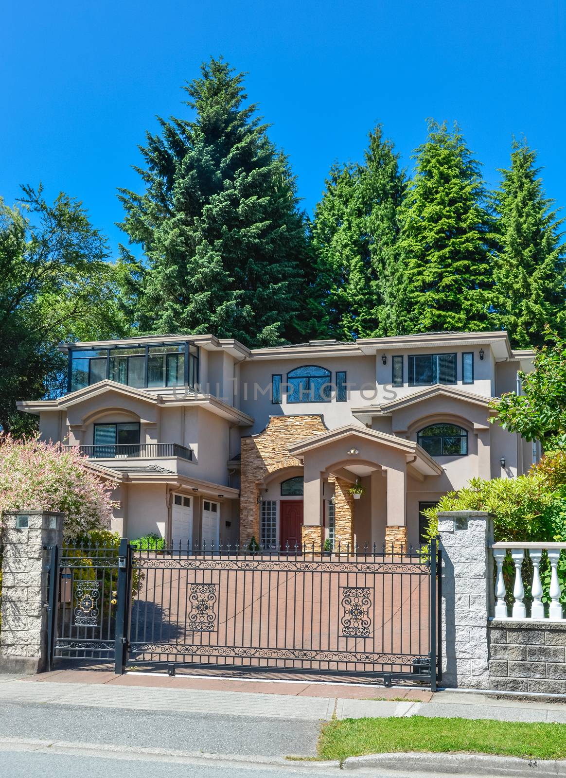 Luxury residential house with double garage and metal gate in front. Beautiful house in suburb of Vancouver on blue sky background