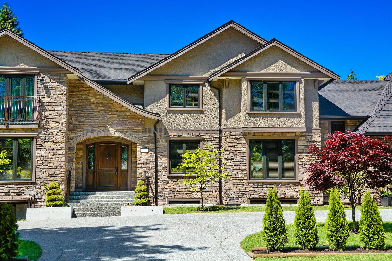 Entrance of luxury family house with green lawn and concrete driveway in front on blue sky background