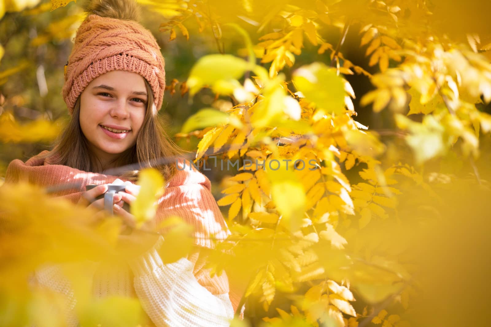 Portrait of pretty nice teenage girl drinking hot cocoa with marshmallows in autumn park