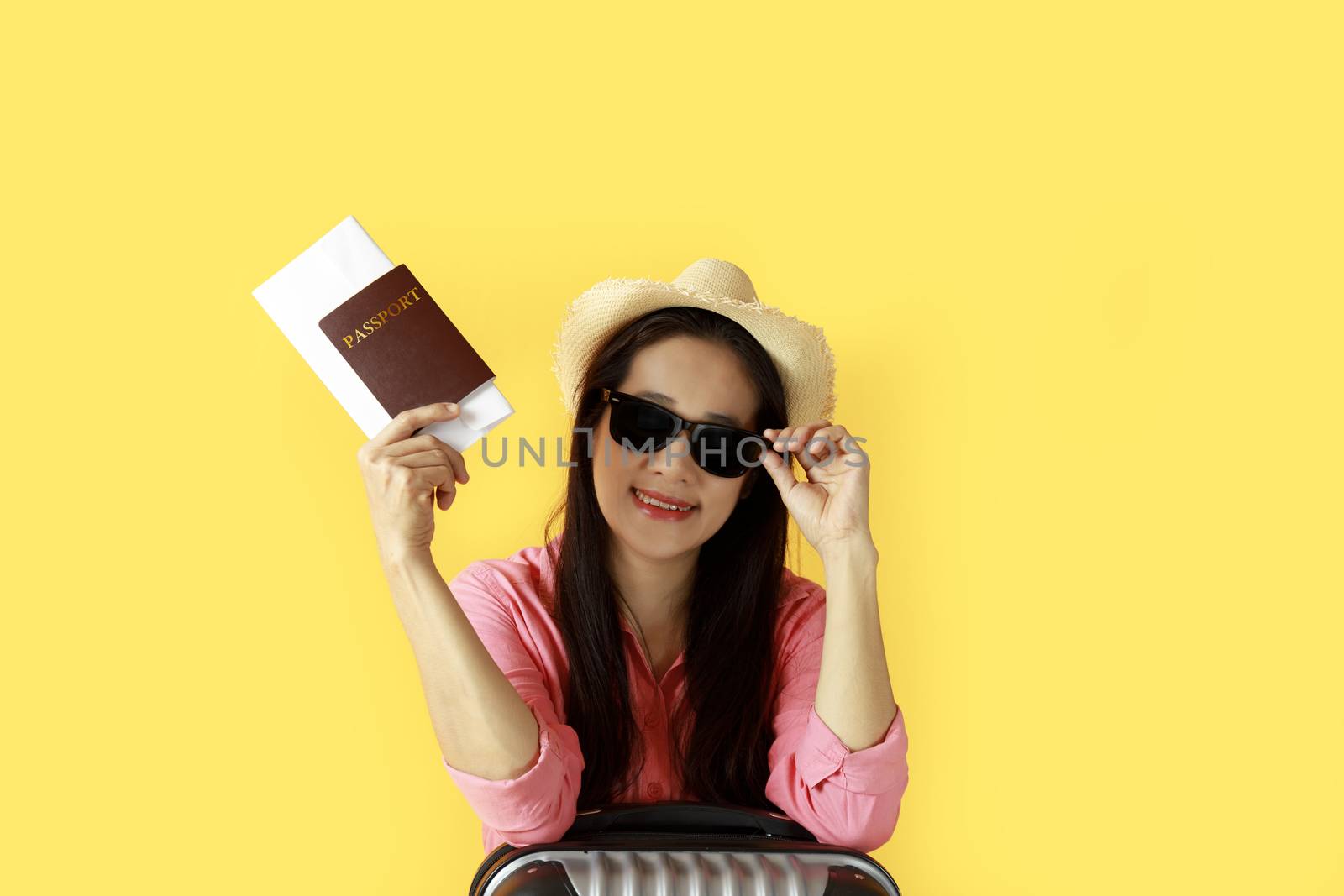 Asian women long hair wear Straw hat, sunglasses in hand holding passport book and travel bag with copy space banner. Young girl ready to travel with suitcase and passport on yellow background. Summer