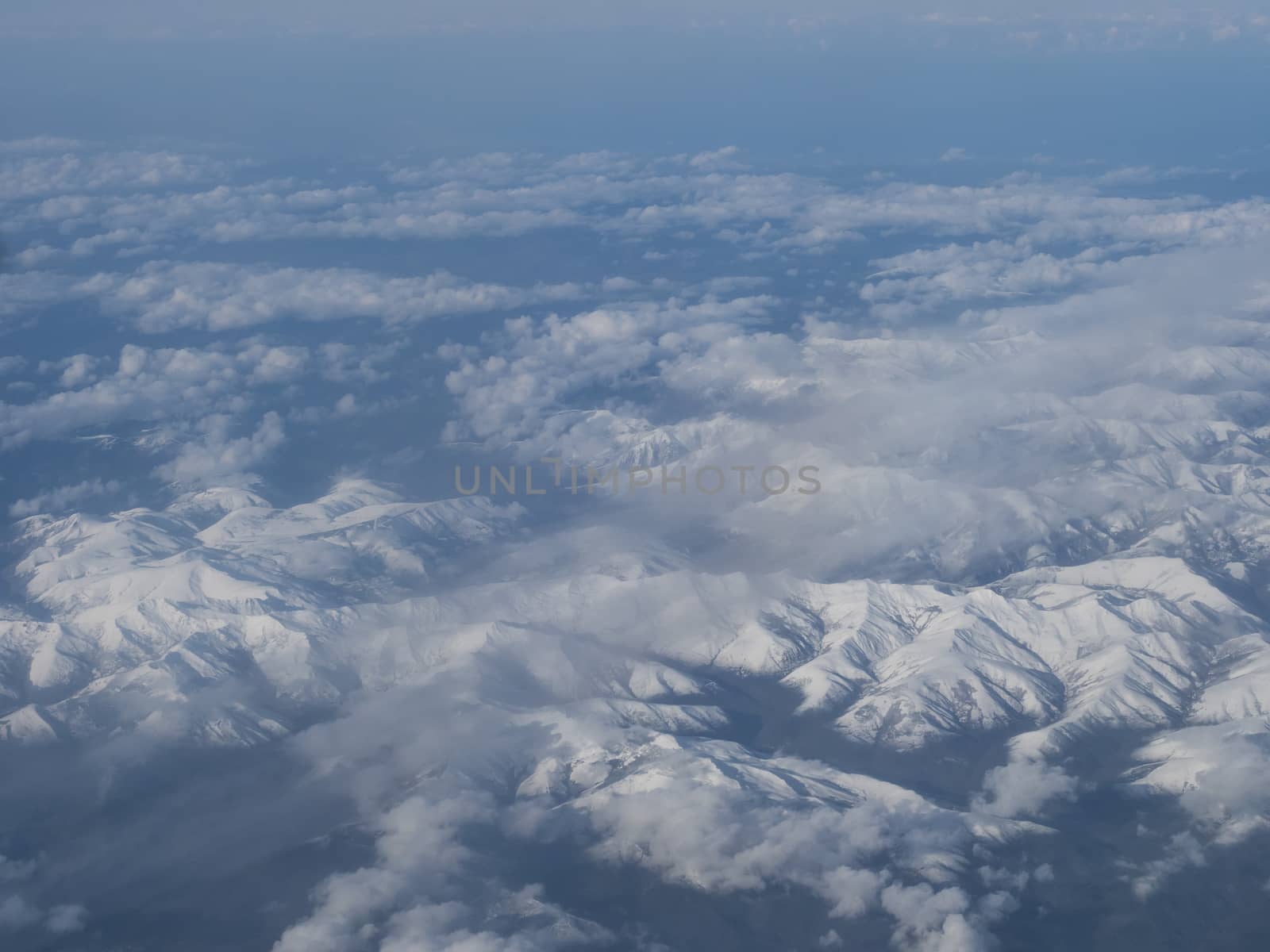 Aerial view of snow covered french and spanish pyrenees with snow covered mountains viewed from an airplane. Blue sky white clouds background.