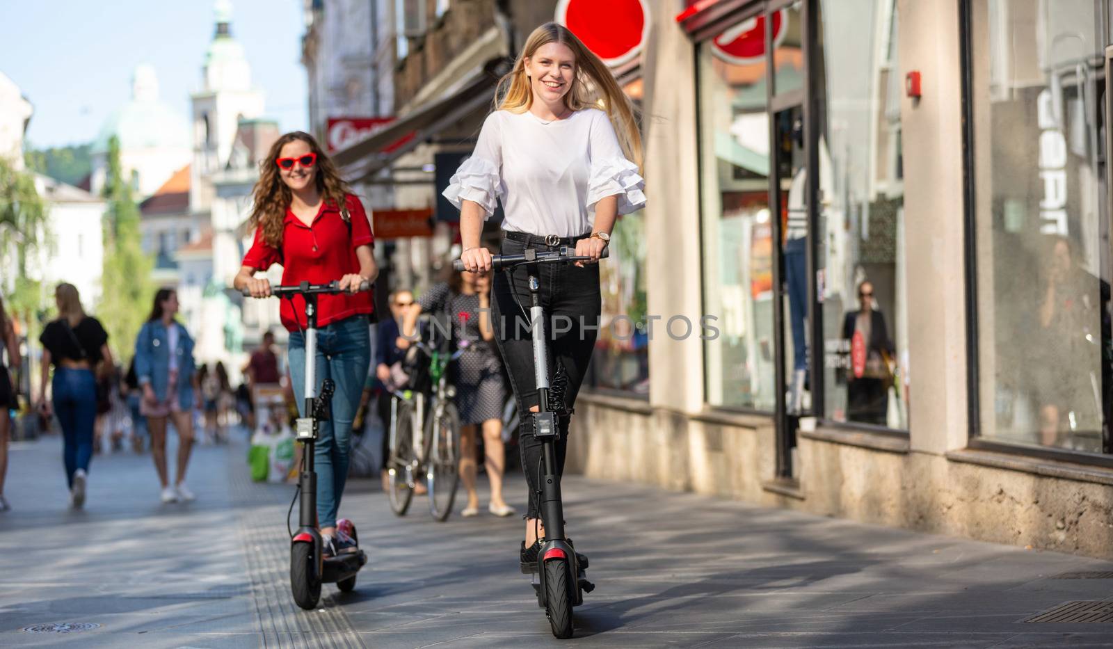 Trendy fashinable teenager girls riding public rental electric scooters in urban city environment. New eco-friendly modern public city transport in Ljubljana, Slovenia by kasto