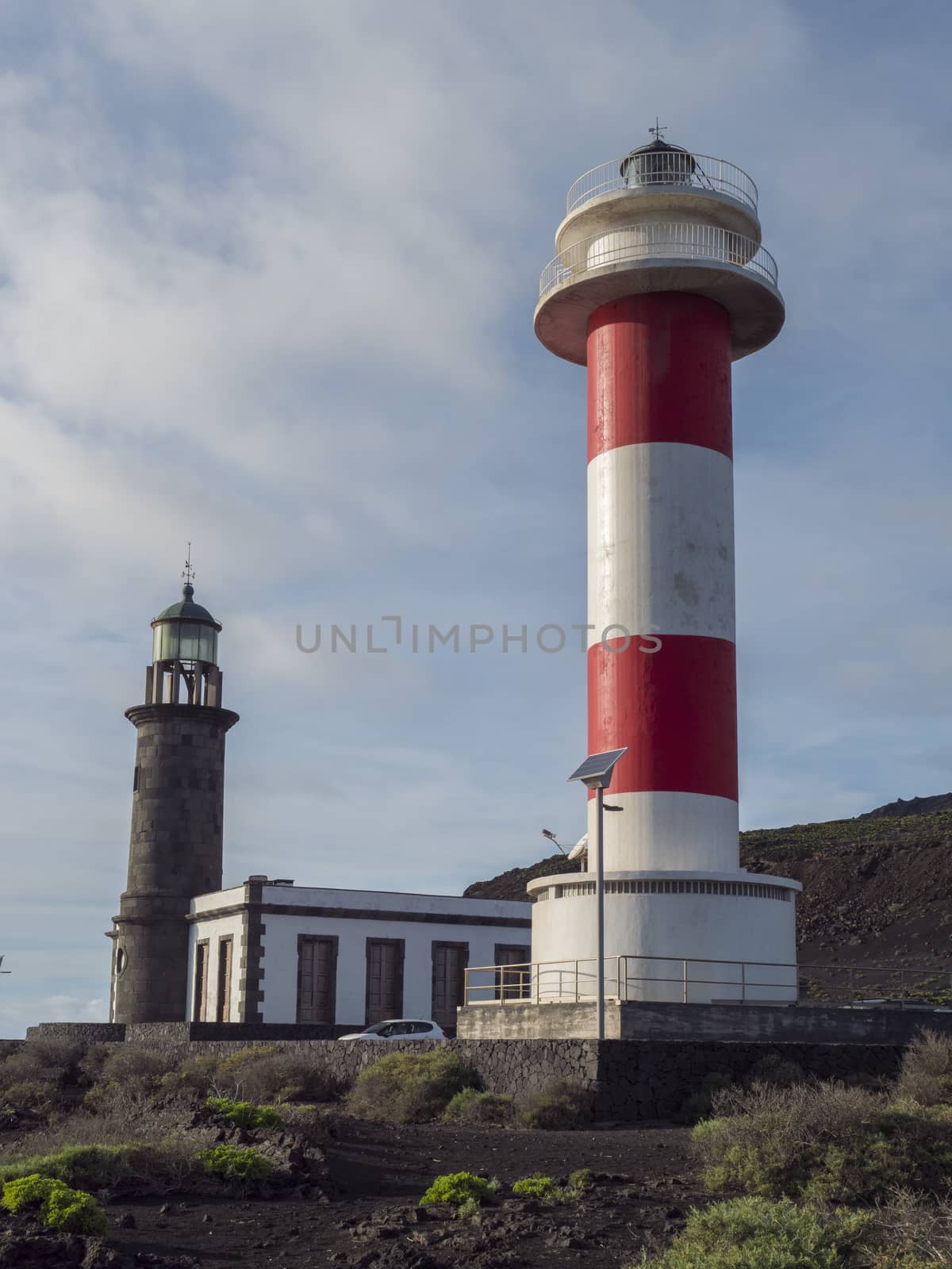 View of two lighthouses, old stone and white-red striped with volcanic rock field at Fuencaliente, La Palma, Canary Islands. Blue sky white clouds background.