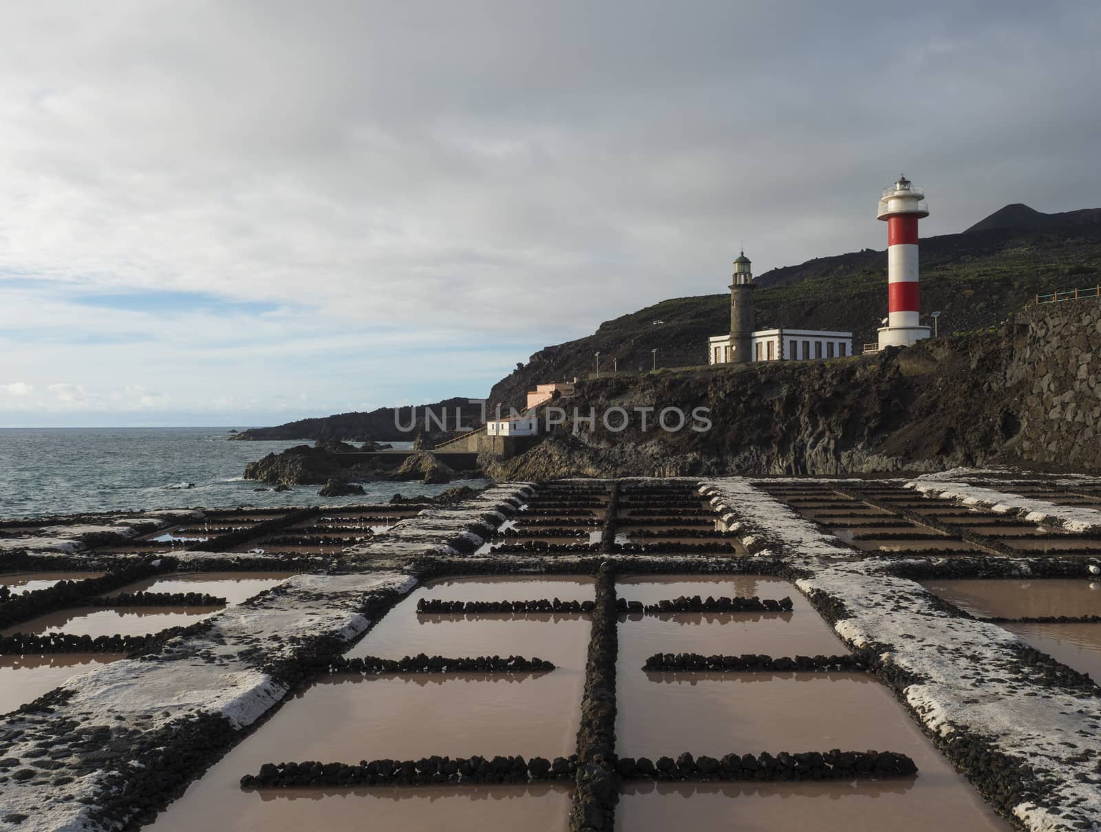 View of Fuencaliente salinas or saltworks and two lighthouse, old stone and white-red striped with volcanic rock field.La Palma, Canary Islands. Ocean, blue sky white clouds