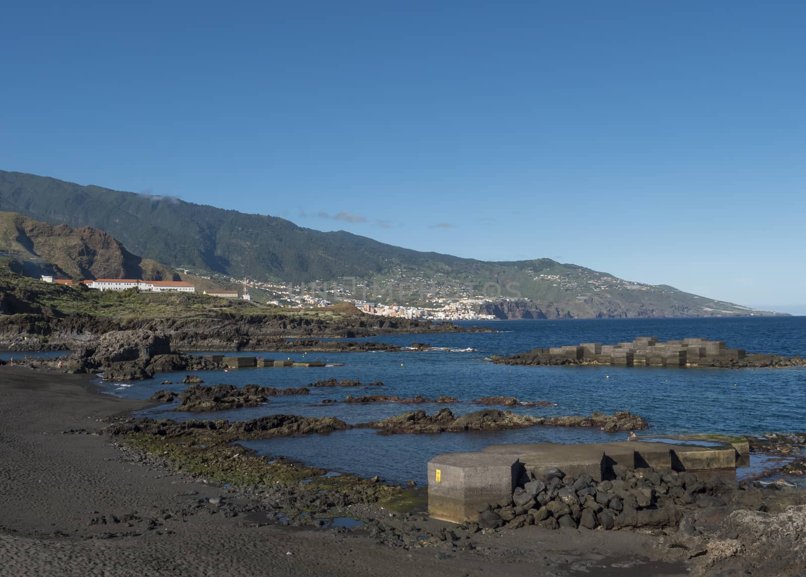 The dark sand beach of the village of Los Cancajos at La Palma, Canary Islands. Lava rock cliffs and Blue sky background