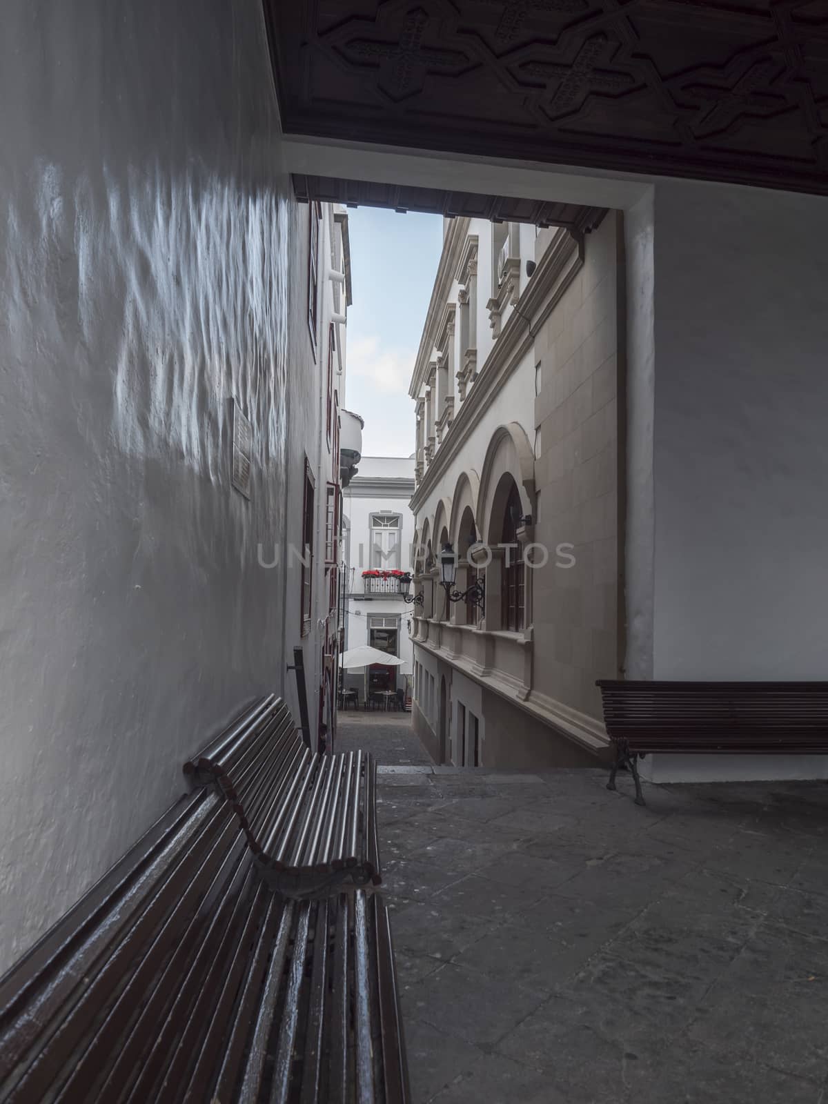 Empty passage to street at Santa Cruz de la Palma old city center with white traditional house and wooden benches. La Palma, Canary Islands, Spain.