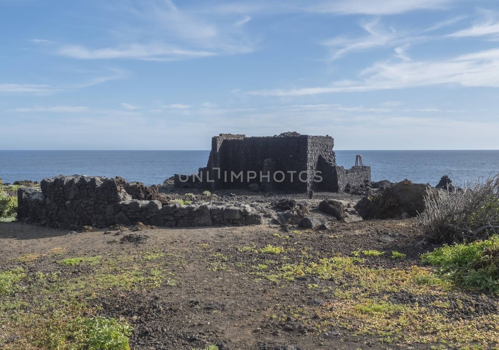 Old lava stone and wooden rustic door, blue house, white apartments, palm trees, green hills and blue sky at Canary islands village