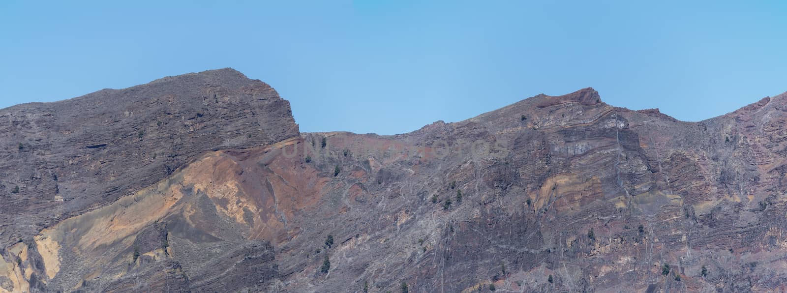 Panoramic view on colorful vocanic rock of crater Caldera de Taburiente with mountainRoque de los Muchachos on the island La Palma, Canary Islands, Spain. Blue sky background.