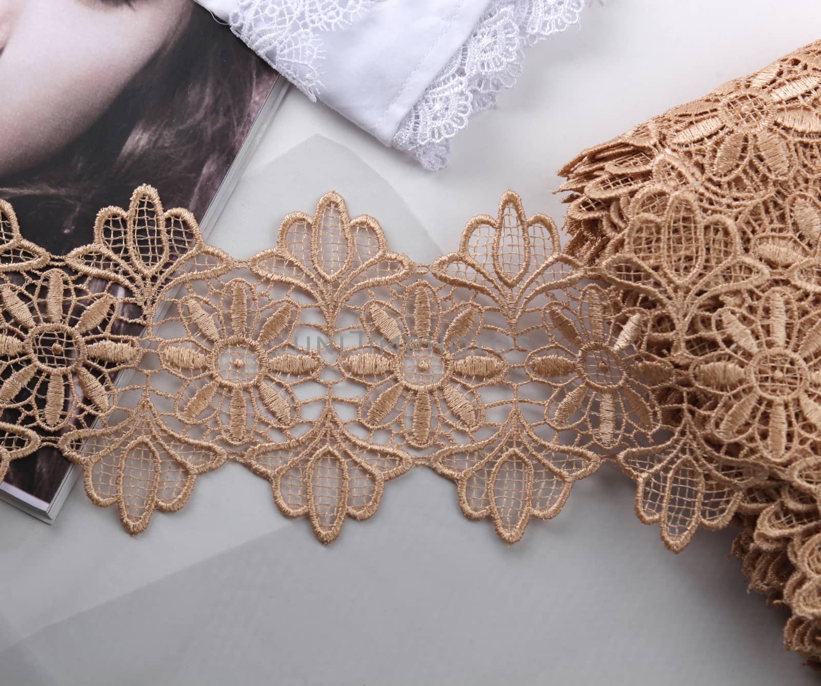 Tapes of beige gentle guipure, beauty lace fabric on light background. Elastic material. Using for Atelier and needlework store.