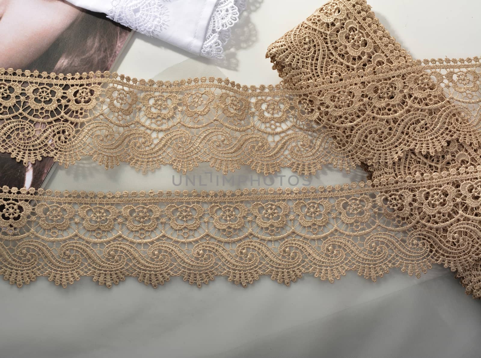 Tapes of beige gentle guipure, beauty lace fabric on light background. Elastic material. Using for Atelier and needlework store.