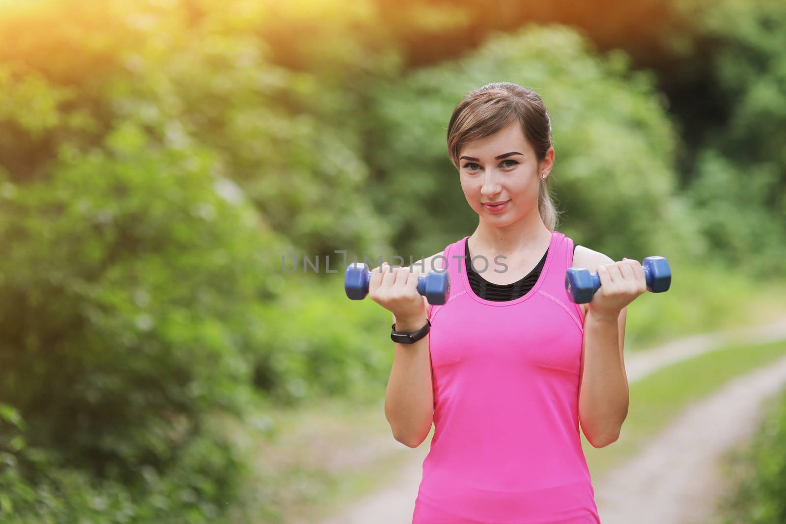 The girl is engaged in sports with weights in nature forest. Healthy fit living by selinsmo