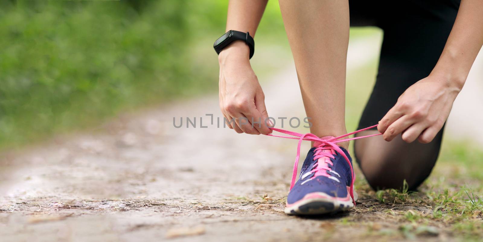 Young fitness woman tying shoelace running sneakers. In the morning forest trail. Motivation healthy fit living. Running shoe of the person running in nature with beautiful sunlight.