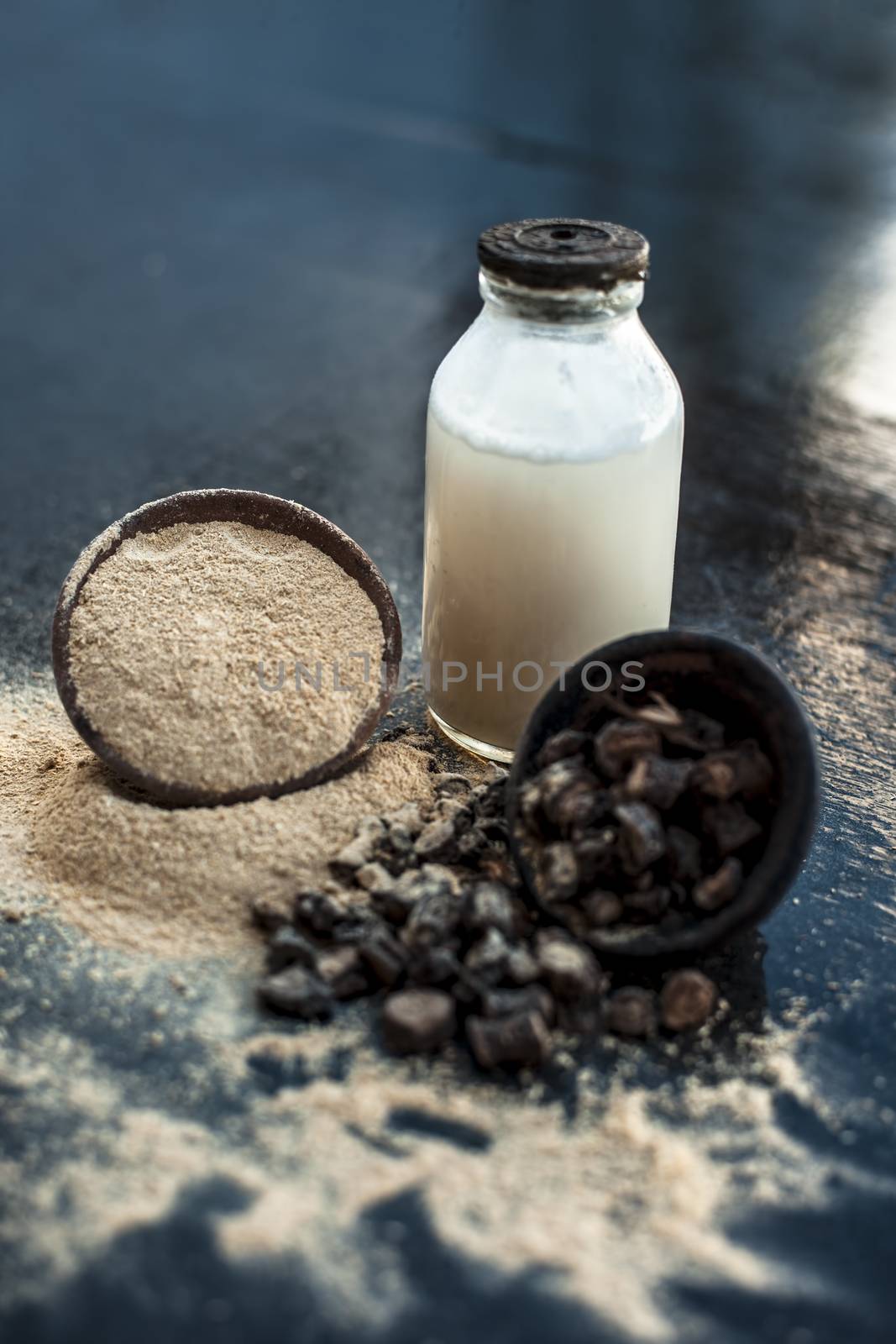 Popular Indian &amp; Asian ayurvedic organic herb musli or Chlorophytum borivilianum or Curculigo orchioides or kali moosli in a clay on wooden surface with a transparent glass bottle filled with milk.