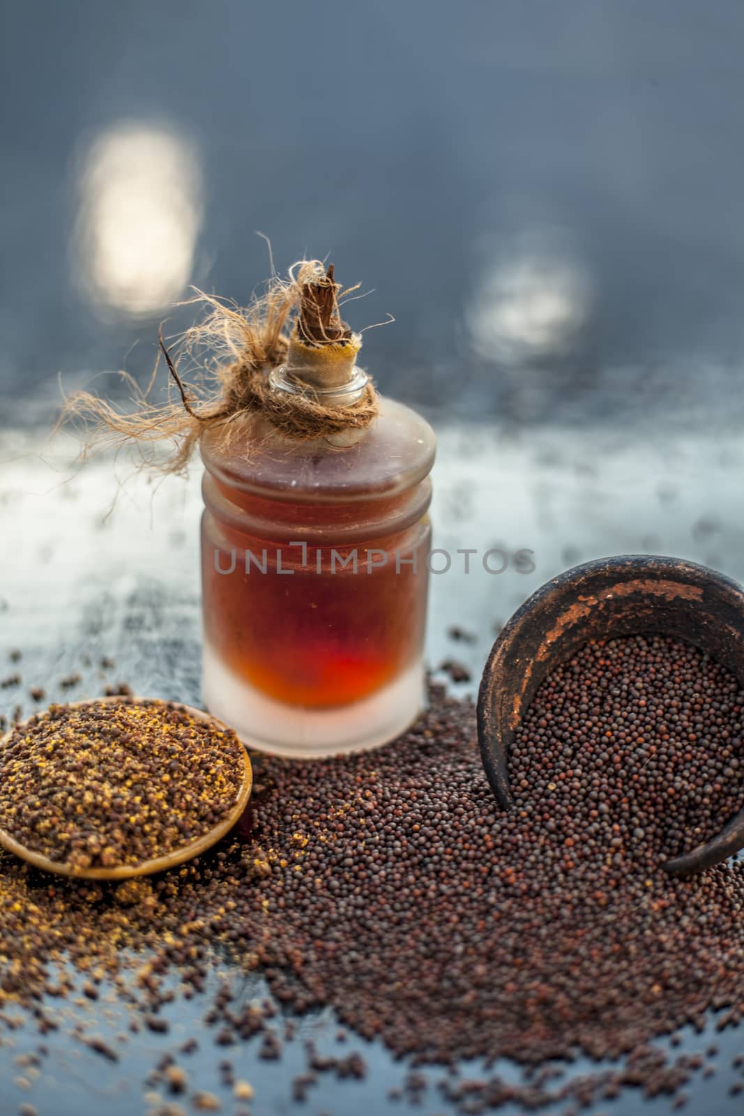 Raw organic herbal spice Mustard seeds or sarso or rai or Brassica nigra, in a clay bowl on wooden surface with its extracted essential oil in a transparent glass bottle.