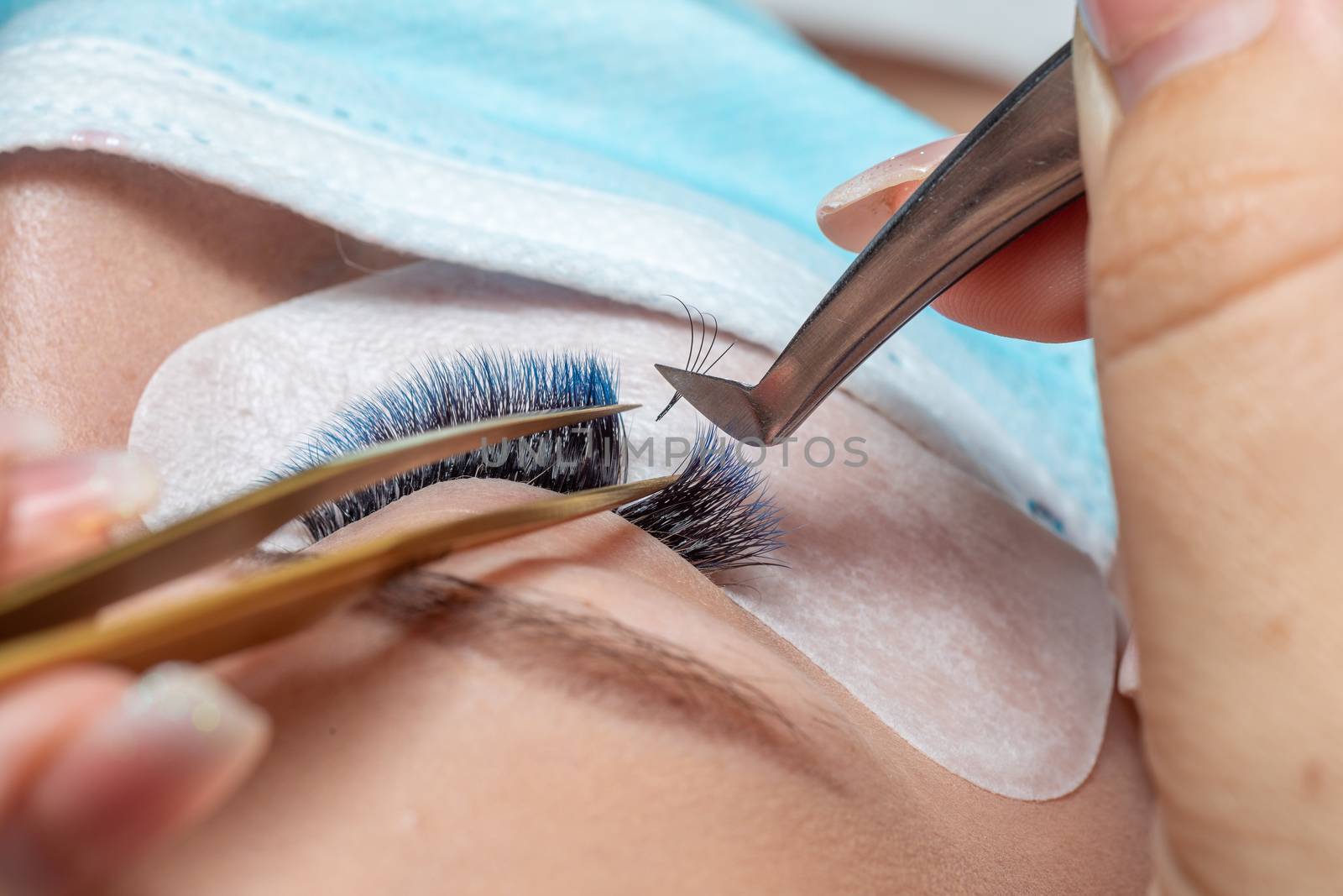 Treatment of Eyelash Extension in blue color Lashes. Eyes with Long Eyelashes and face with facemask