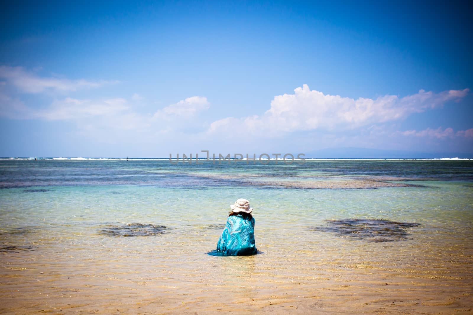 Beach scene with woman relaxing looking out to sea on a Sanur beach in Bali, Indonesia