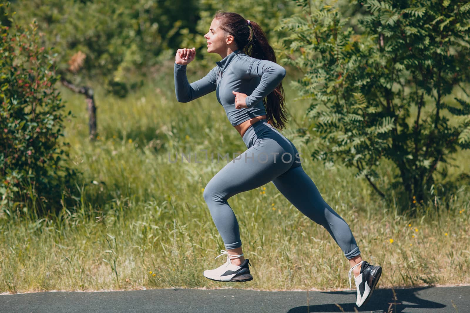 Running girl in city park. Young positive woman runner outdoor jogging.