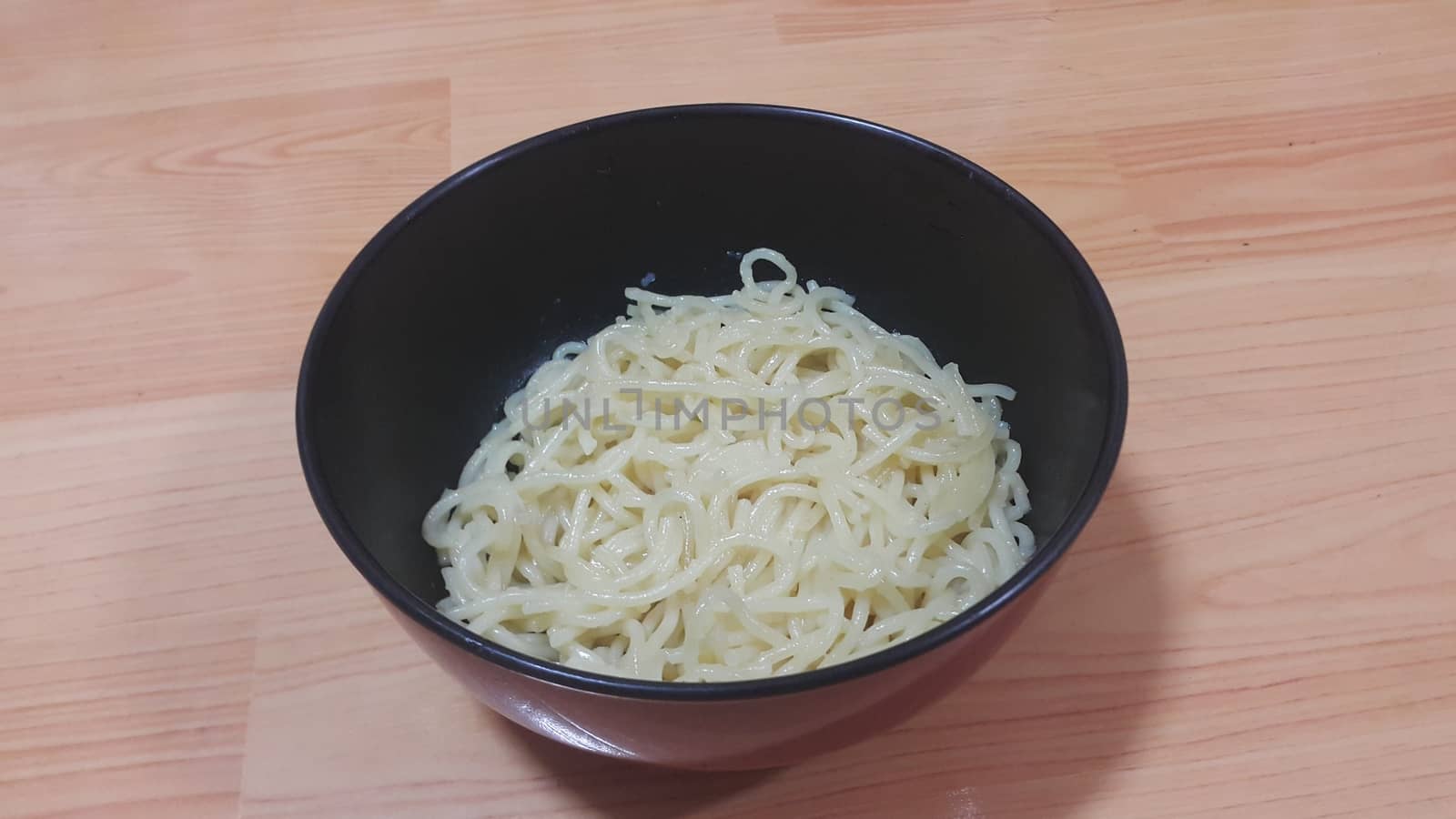 close up view of swirling noodles or spaghetti pasta in a bowl over wooden floor. Food background for fast foods