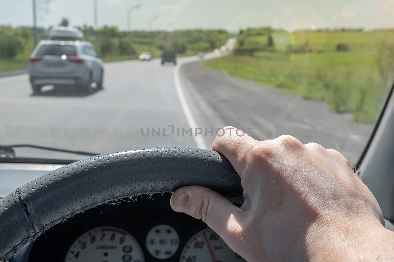 driver hand on the steering wheel of a car that is passing on a country highway by jk3030