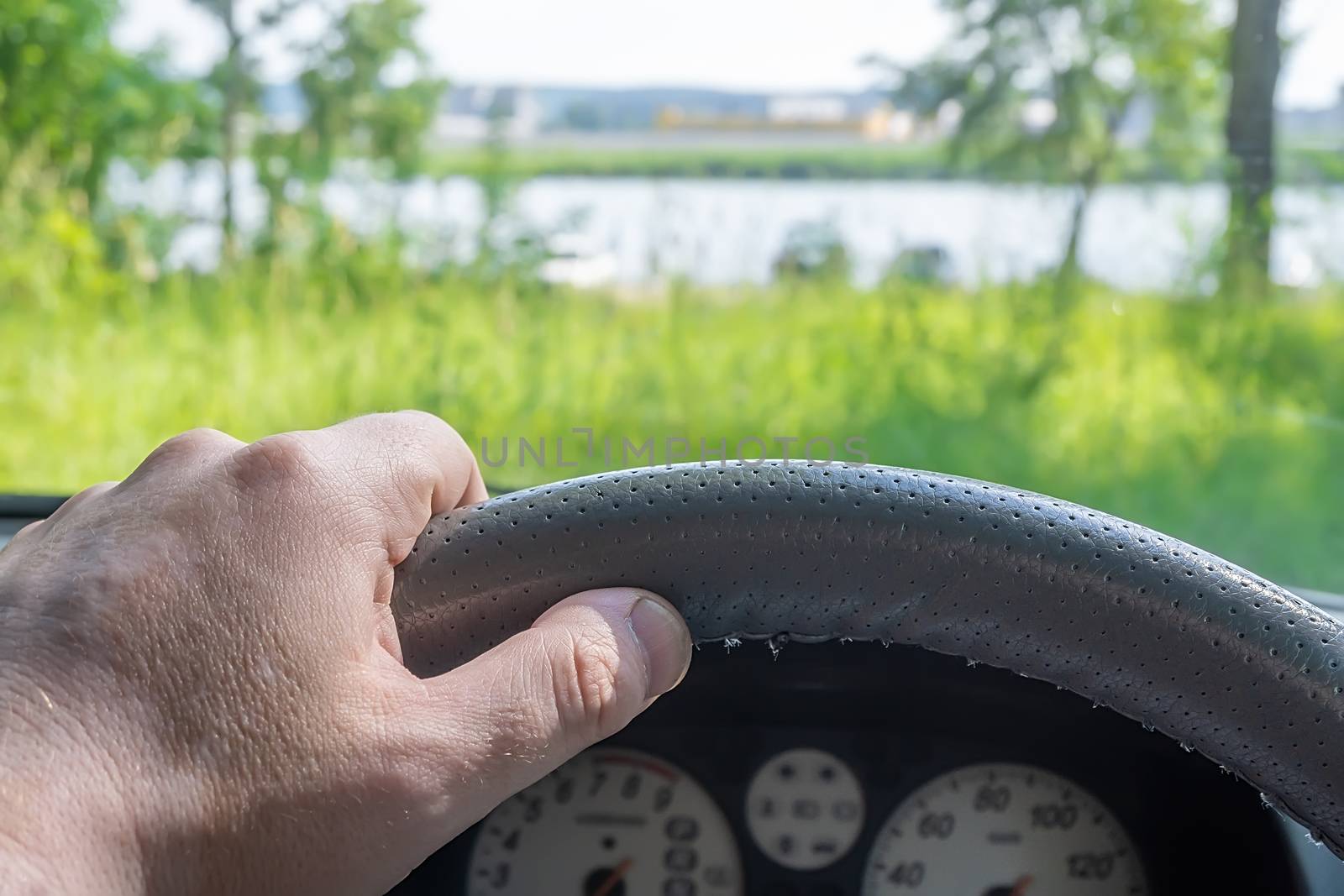 view of the driver hand at the wheel of a car against the background of nature and the river outside the city