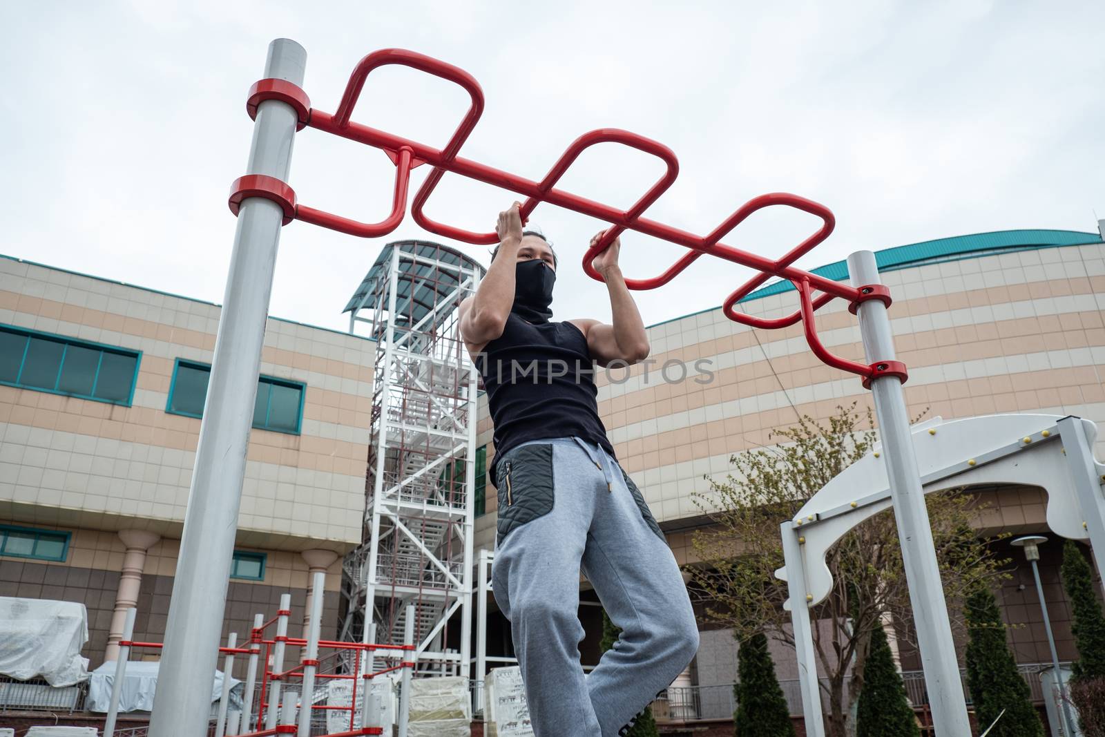 The guy is pushing up on the bars, in a black T-shirt and mask, in quarantine