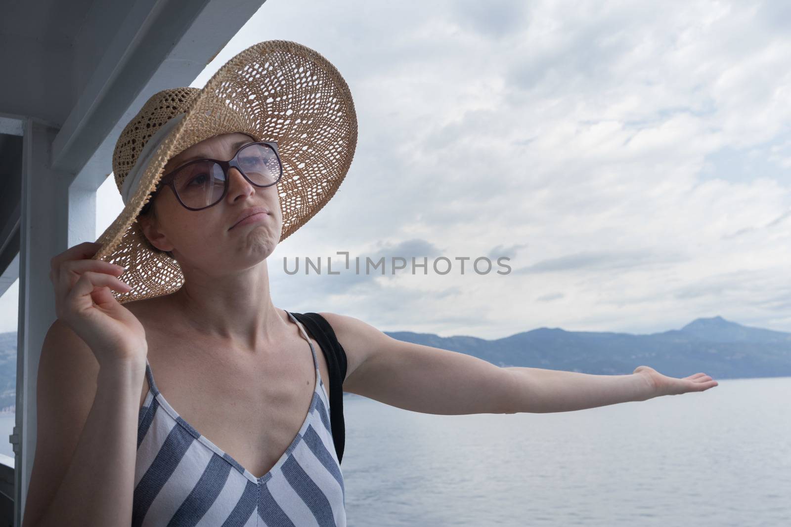 Disappointed female tourist on summer cruss ship vacation, checking if it rains, looking angry at overcast cloudy sky. Allways take the weather with you on summer vacations by kasto