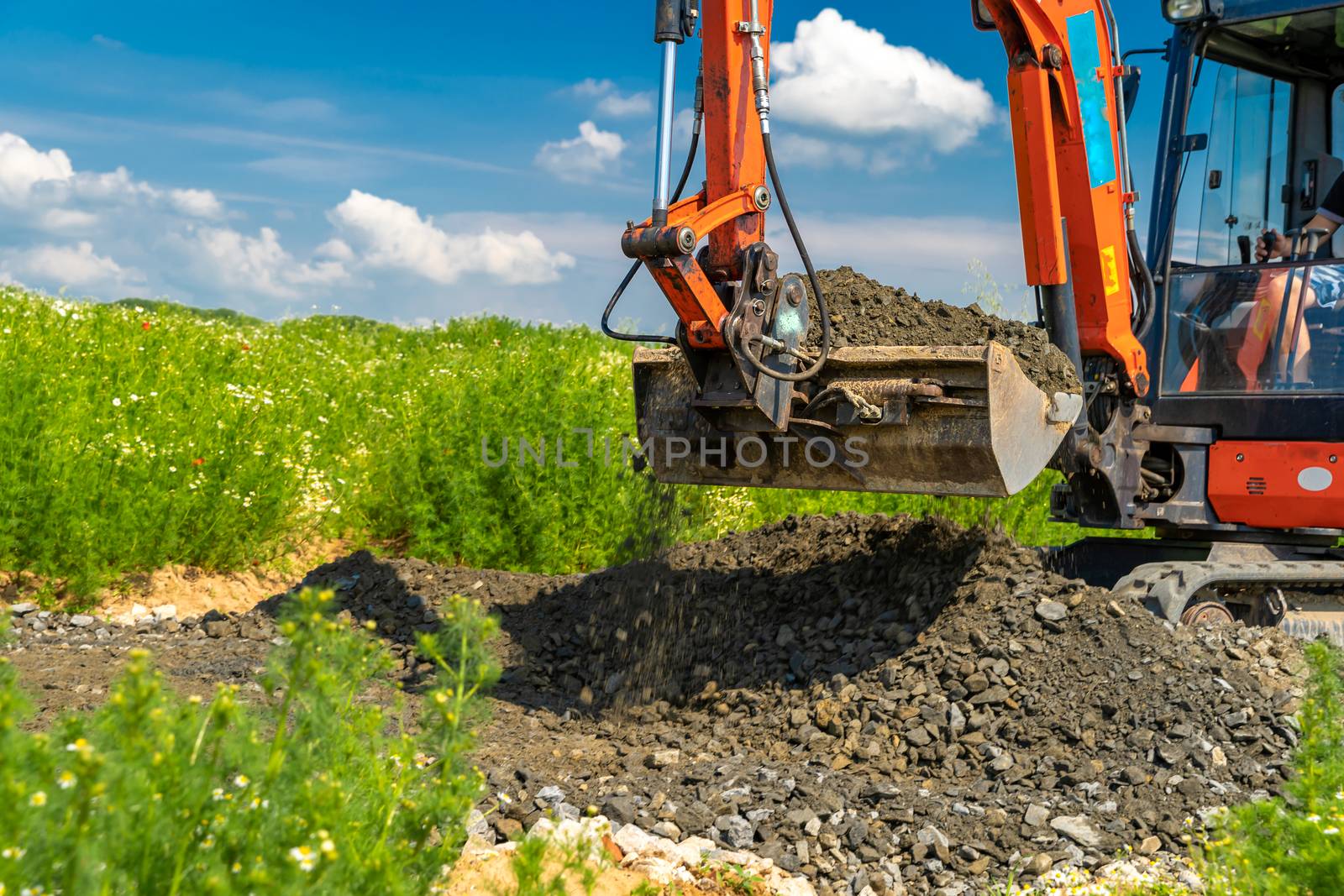 A small excavator is building a new road on a green field