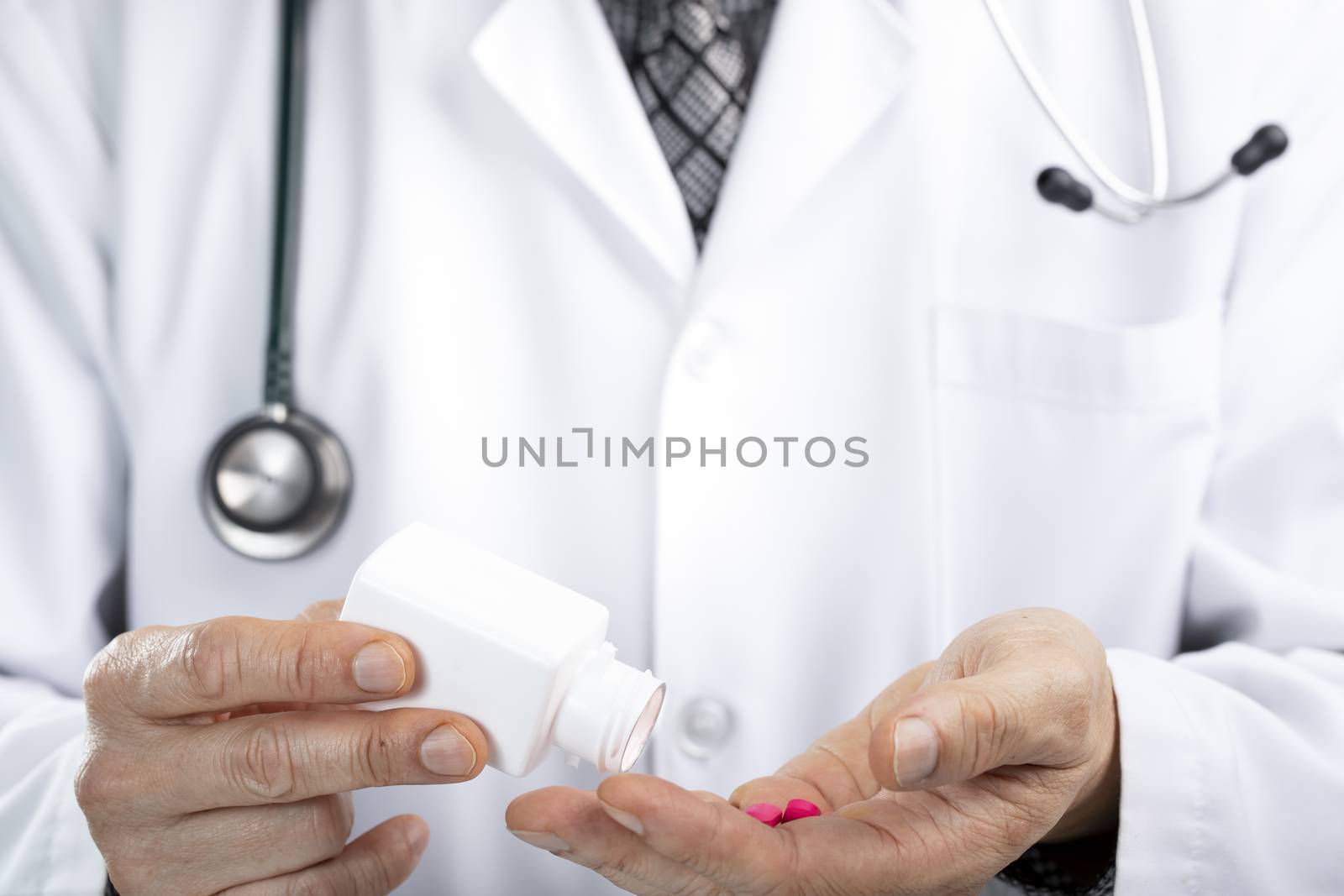 A male doctor taking pills from a white plastic prescription bottle or container Medical administration concept. Asian ethnicity.