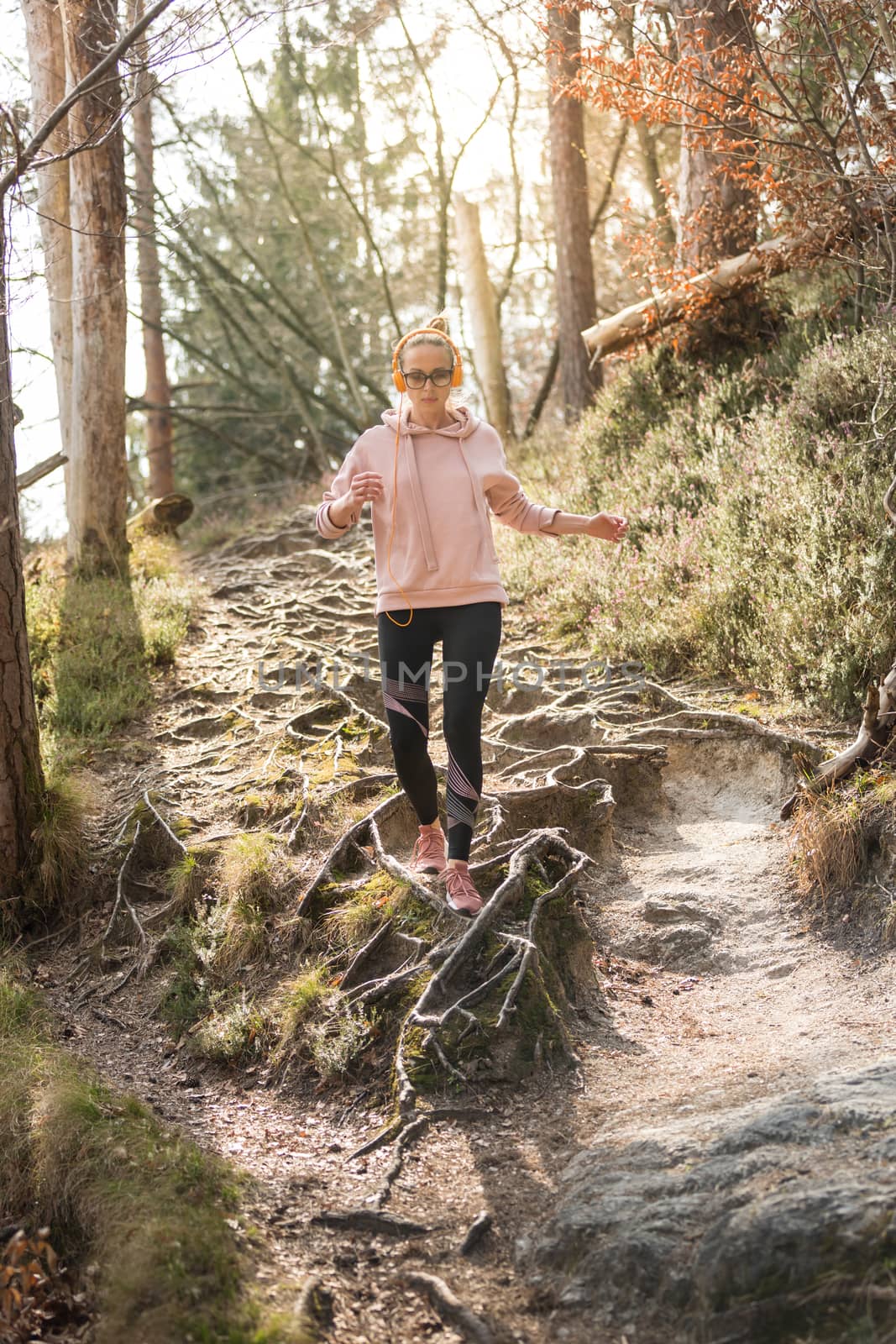 Active sporty woman listening to the music while running in autumn fall forest. Female runner training outdoor. Healthy lifestyle image of young caucasian woman jogging outside by kasto