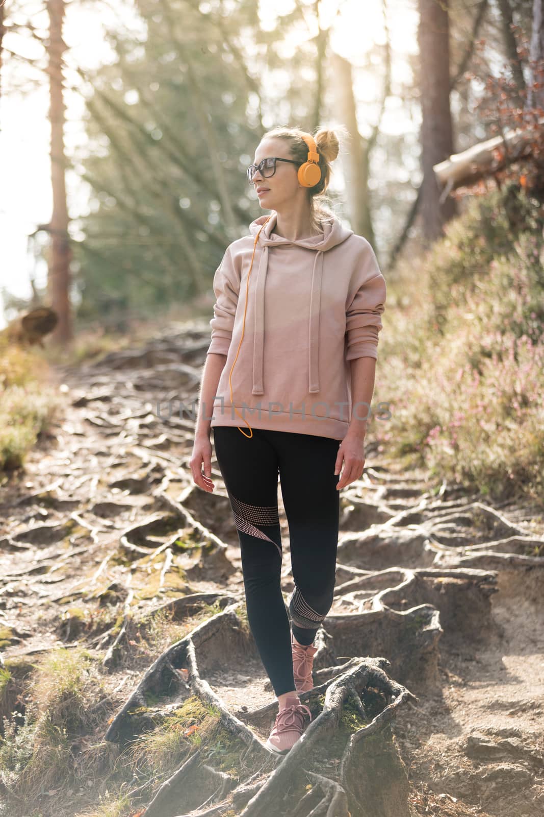 Active sporty woman listening to the music while hiking in autumn fall forest. Female jogger training outdoor. Healthy lifestyle image of young caucasian woman walking on hiking trail in nature by kasto