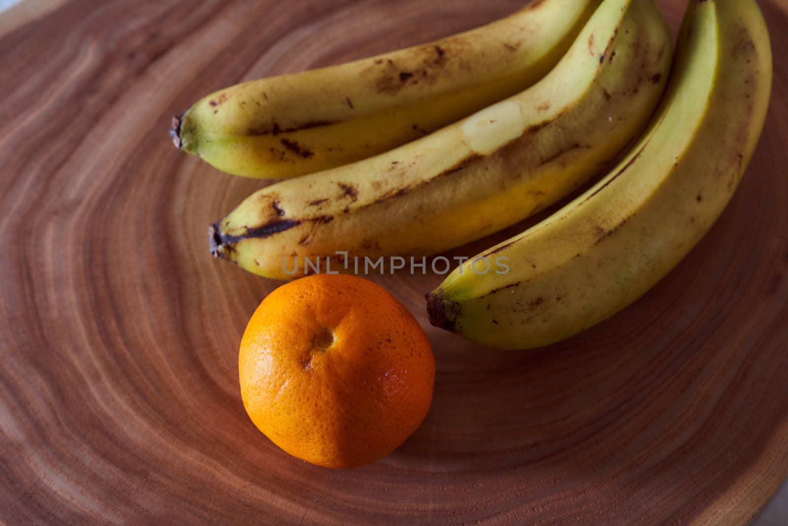 A yellow banana and orange mandarin lies on a slice of a tree. Wooden background. High quality photo